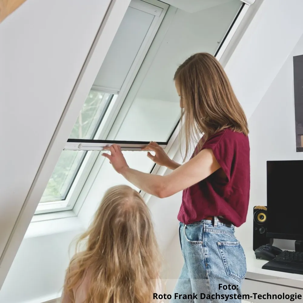 Eine Mutter zieht das Insektenschutzrollo des Dachfensters herunter